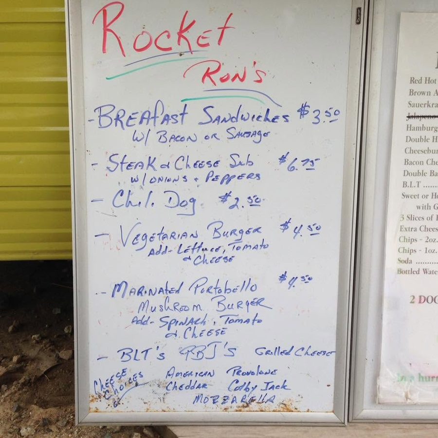 Rocket Ron's handwritten menu board propped against the yellow siding of the food truck